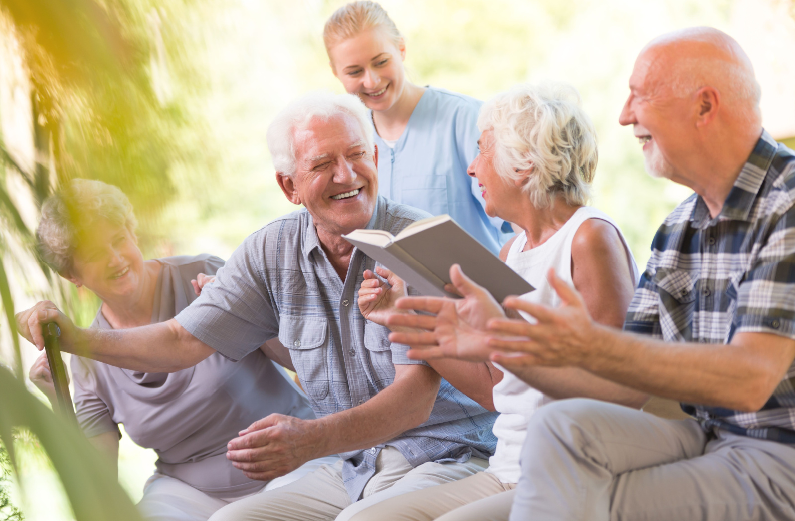 A senior man with a cane with a nurse and other seniors, smiling and looking directly at the camera.