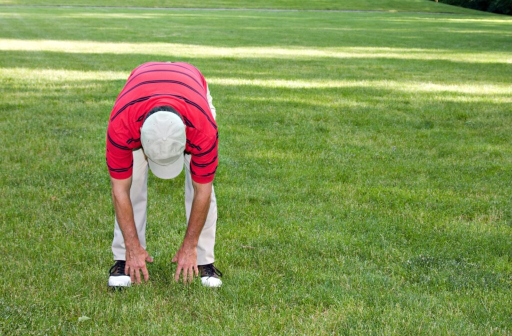 A person stretching by bending forward to touch their toes on a grassy field.