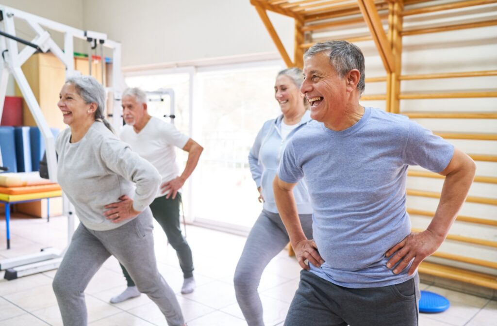 Older adults in a group exercise session, smiling and performing stretches in a fitness studio.
