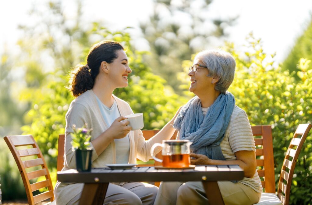A senior shares a cup of tea outdoors with an adult child during a visit to their independent living community