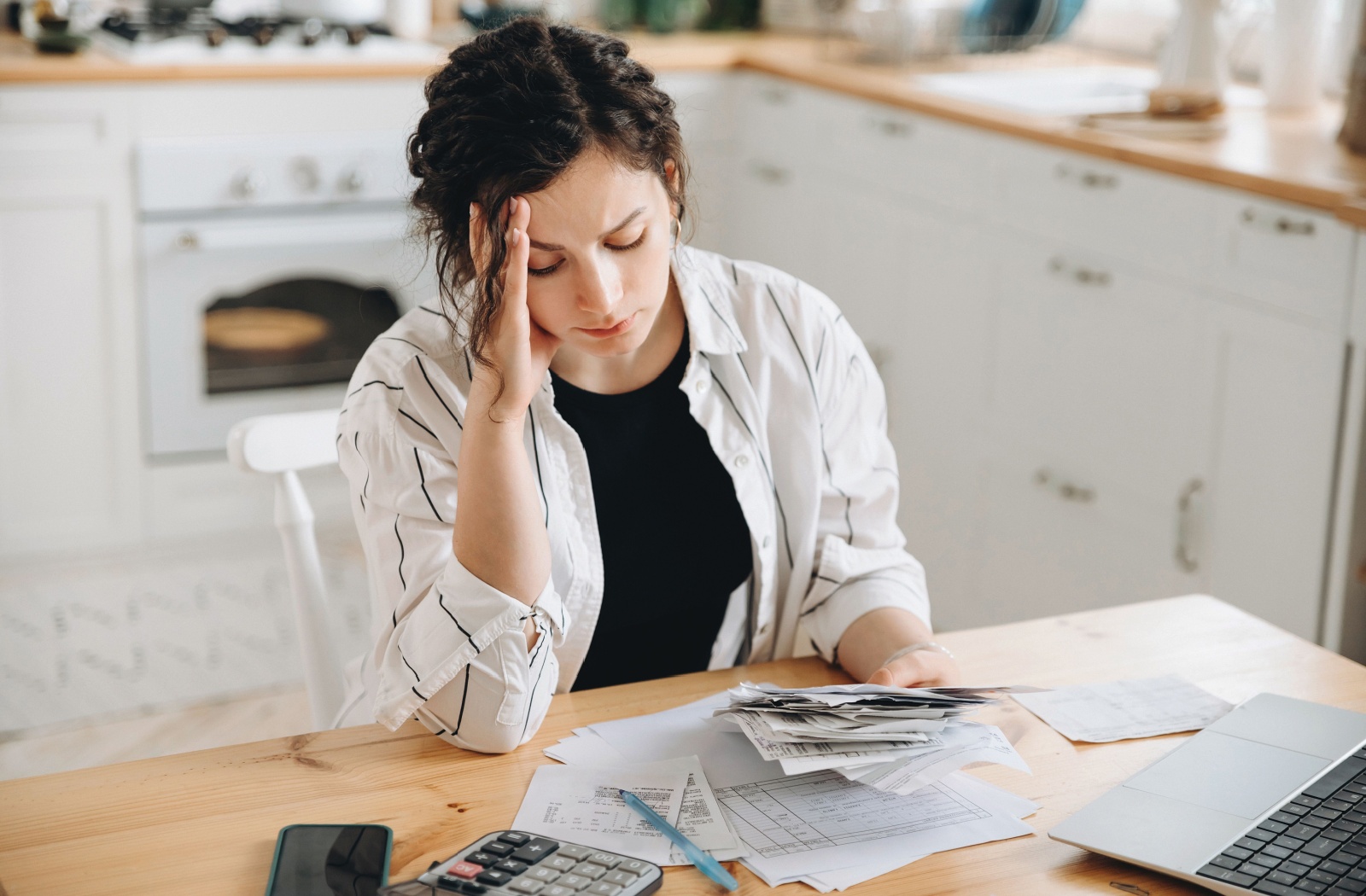 An adult reviews paper copies of bills associated with the costs of caring for an older parent, worried about affording it