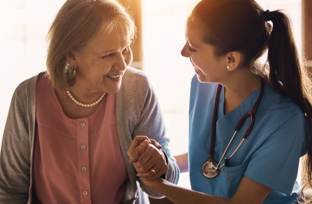 A smiling senior leans on a professional caregiver for support as the sun sets on a beautiful day in senior living