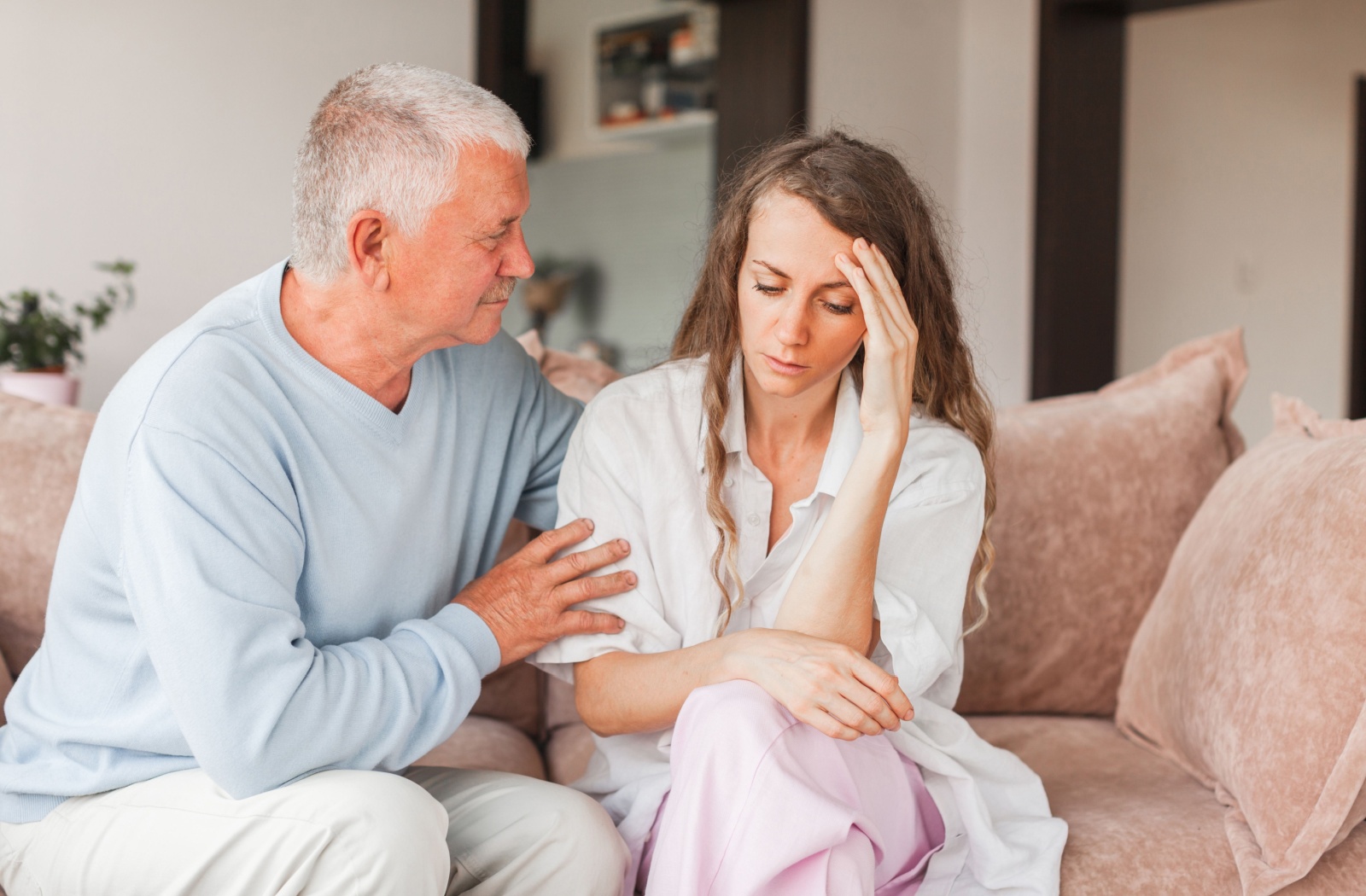 An older adult comforts their stressed adult child while sitting together on a couch in assisted living