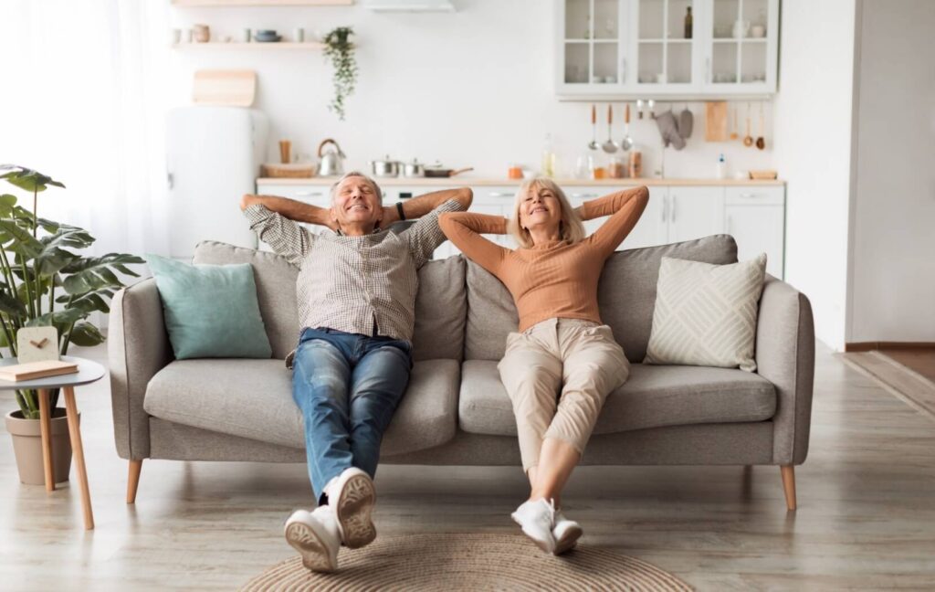 A senior couple relax on the couch in their new independent living home.