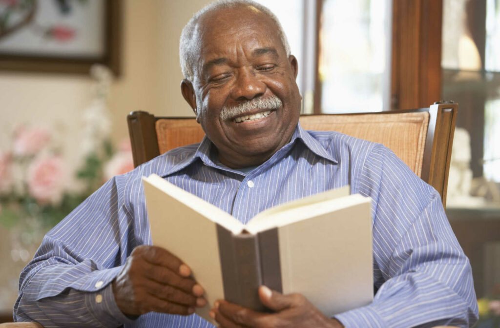 A senior man sitting in a chair reading a book.