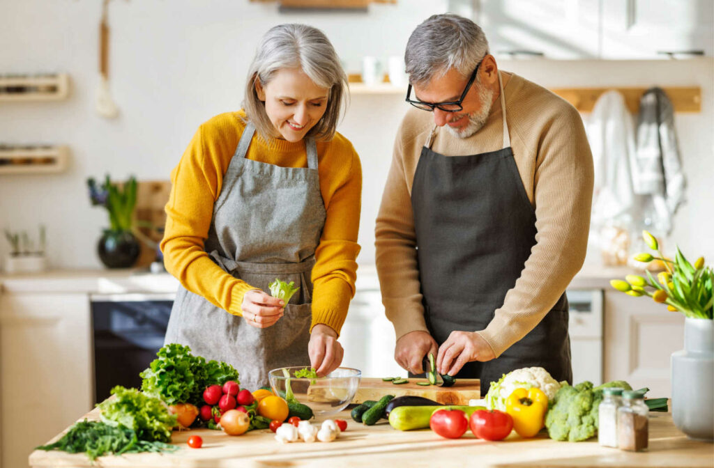 A senior couple standing at a table full of various vegetables preparing a salad.