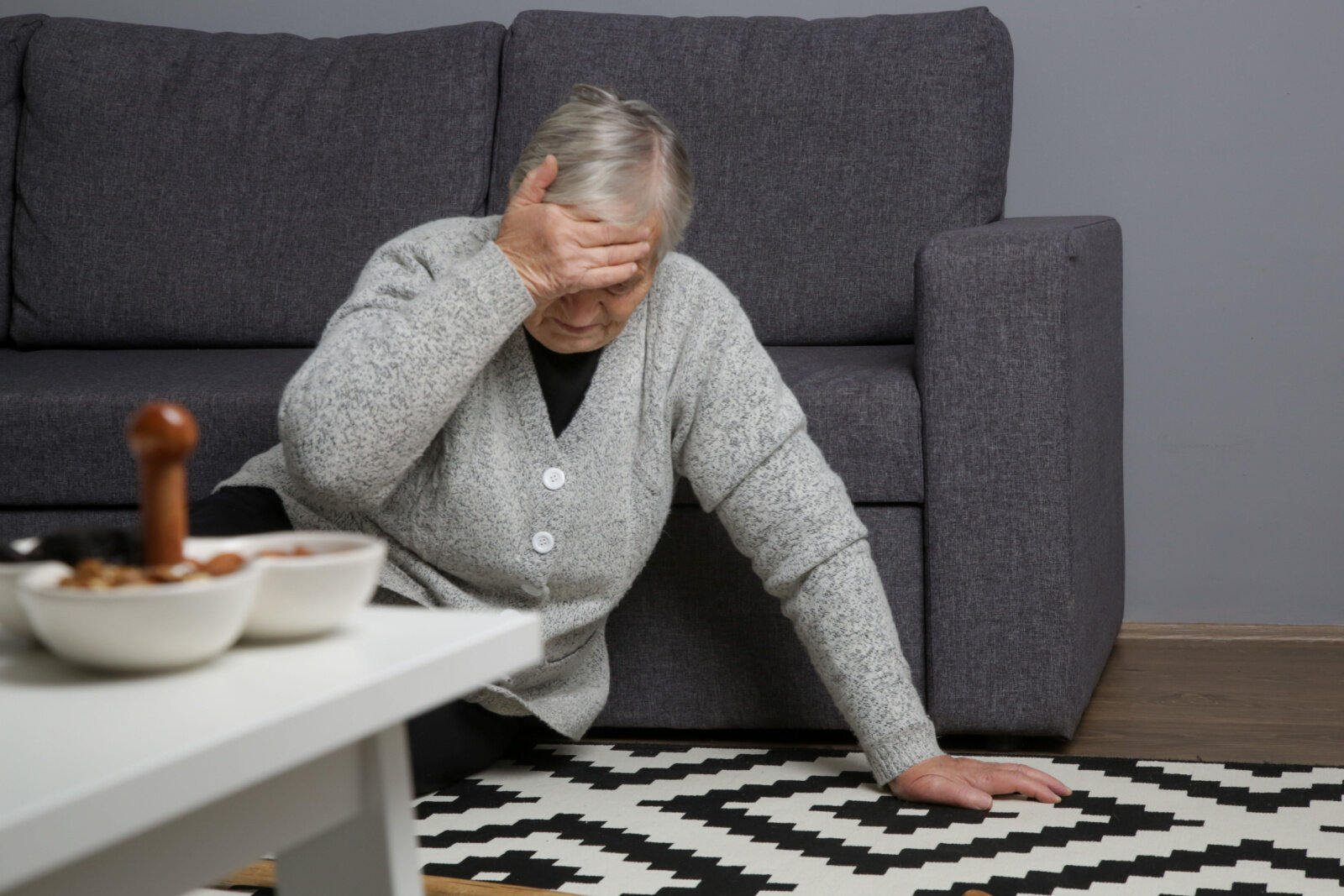 A senior woman fell on the floor after she try to stand from sitting on the couch.