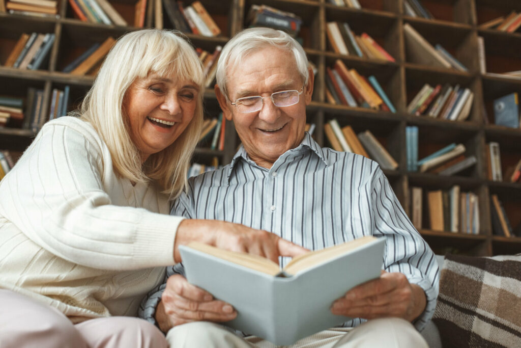 Senior couple smiling and reading a book by sitting on the couch.