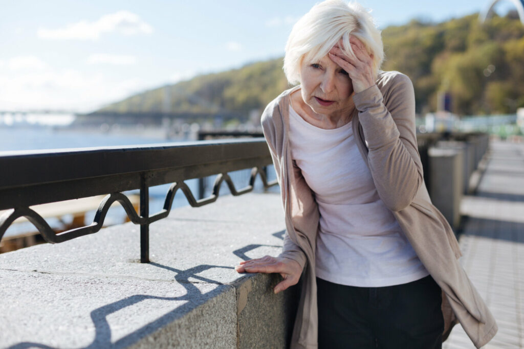 Senior woman is leaning on a barrier and touching her forehead while suffering from a vertigo.