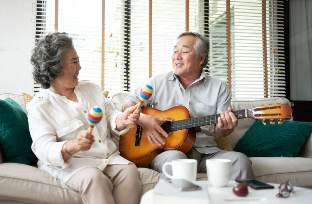 A senior couple playing a guitar and maracas together in the living room.