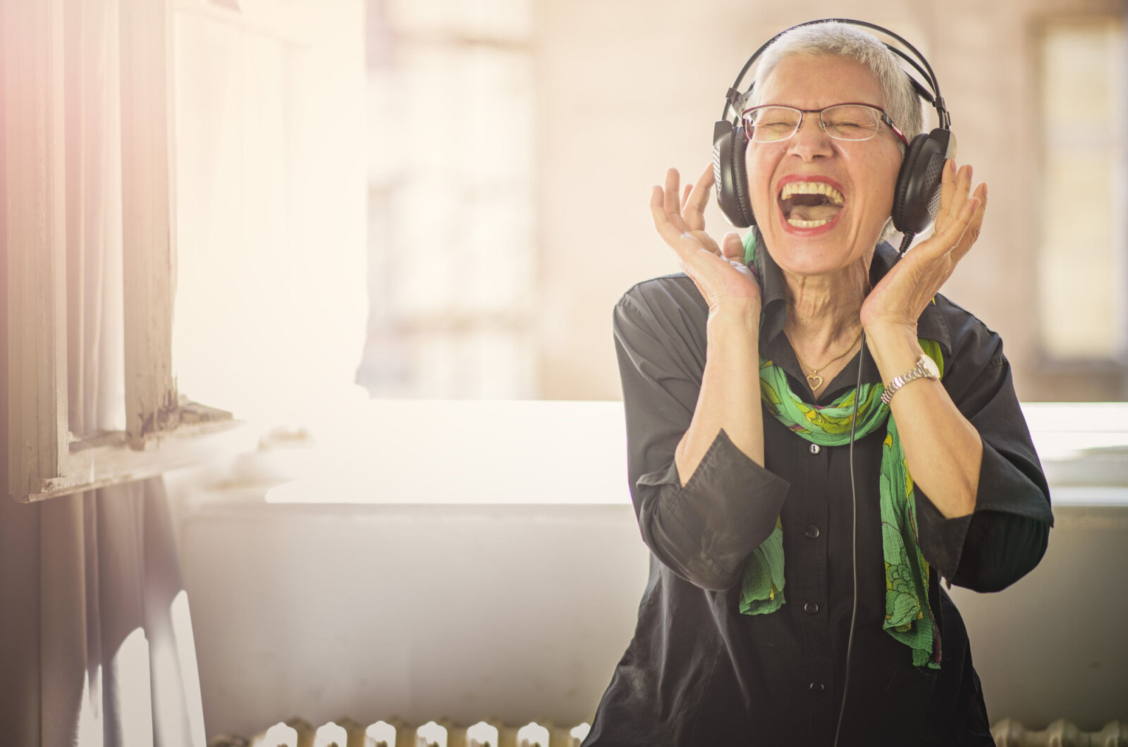 A senior woman listening to her favorite music on a big headphone,  singing along with the music.
