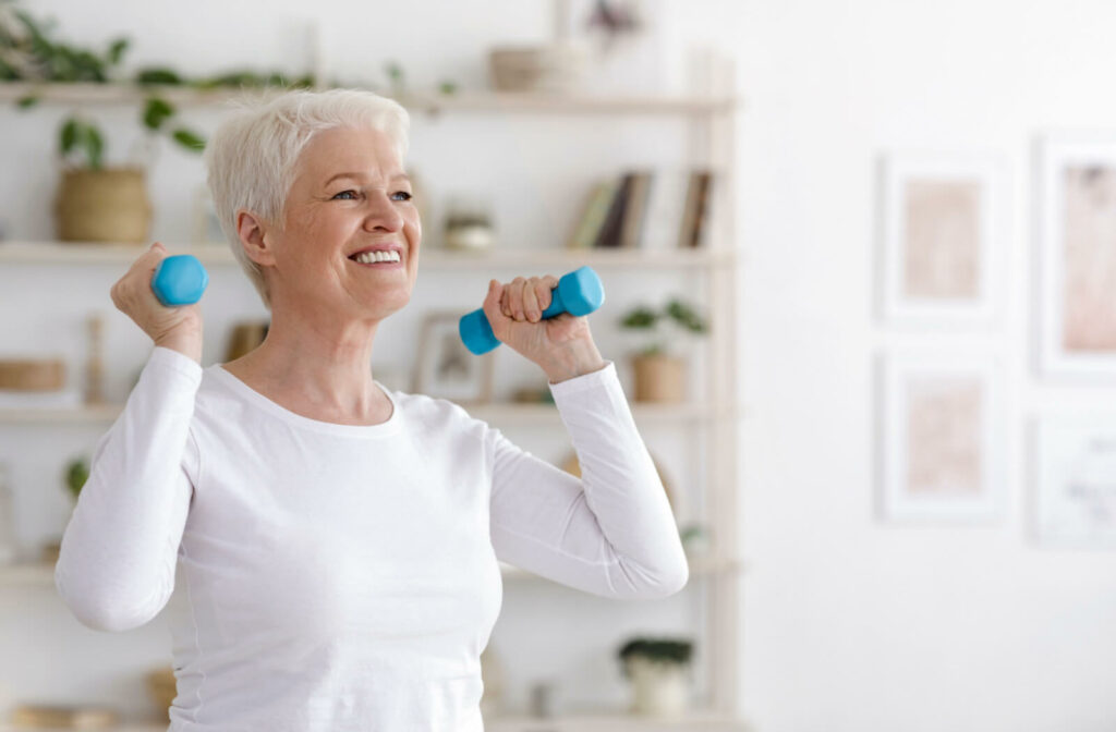 A female senior with gray hair holding a dumbbell and exercising in a senior living facility.