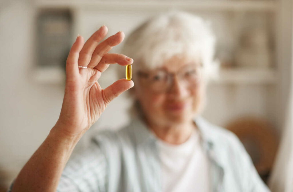 A senior woman with glasses and white hair holding a fish oil pill.
