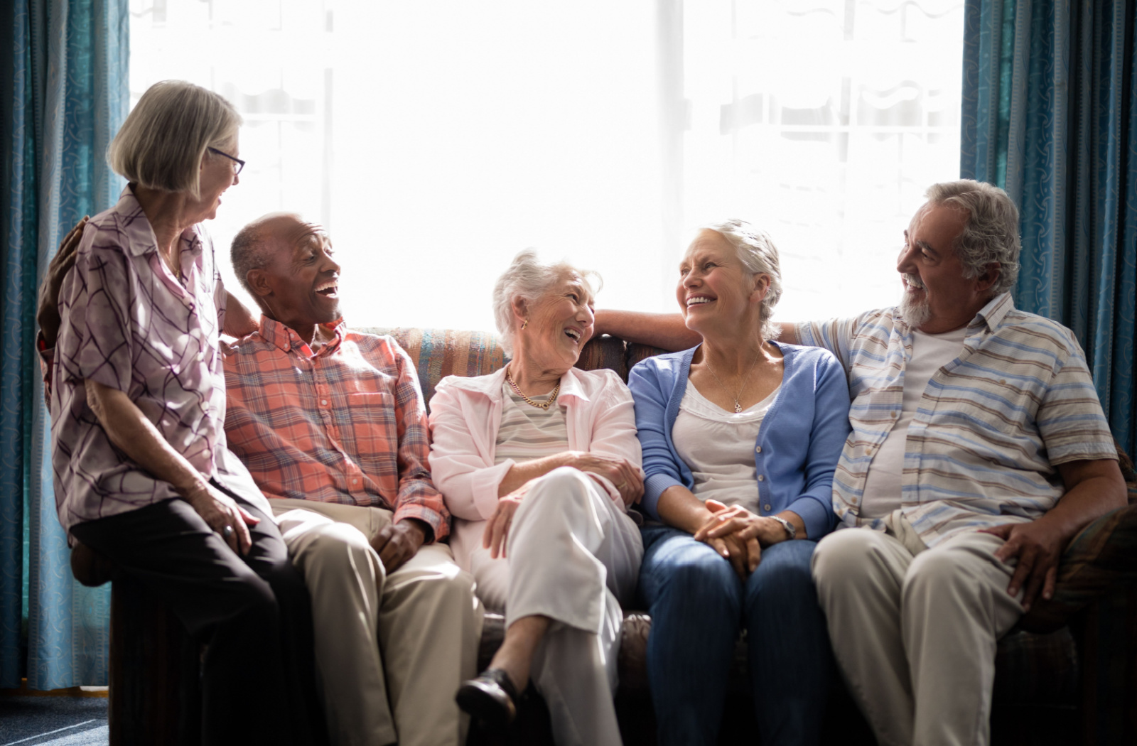 Group of seniors sitting around a couch laughing.