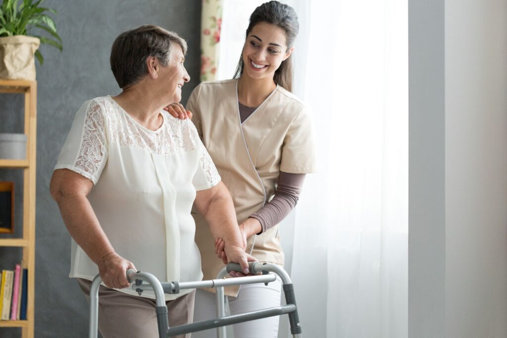 A nurse smiling while she helps a senior woman use her walker.