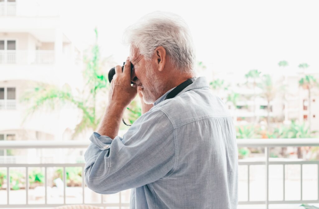 A side-shot of a senior man with a camera to his eye taking a photo from his balcony in senior living.