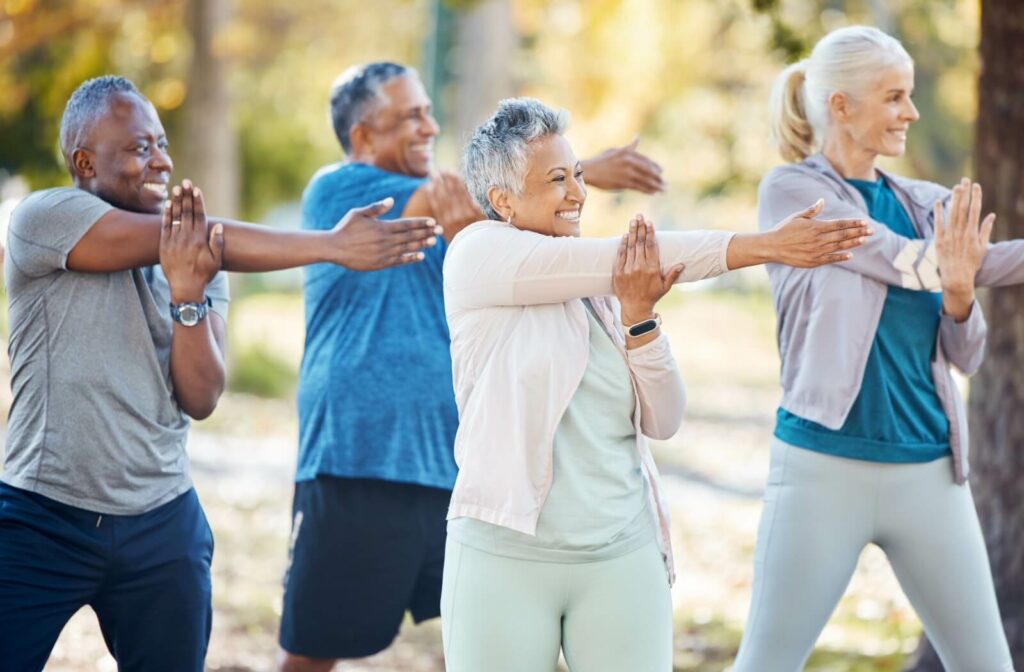 A group of 4 seniors stretching their arms to the side during an exercise class in the park to regain lost muscle mass.