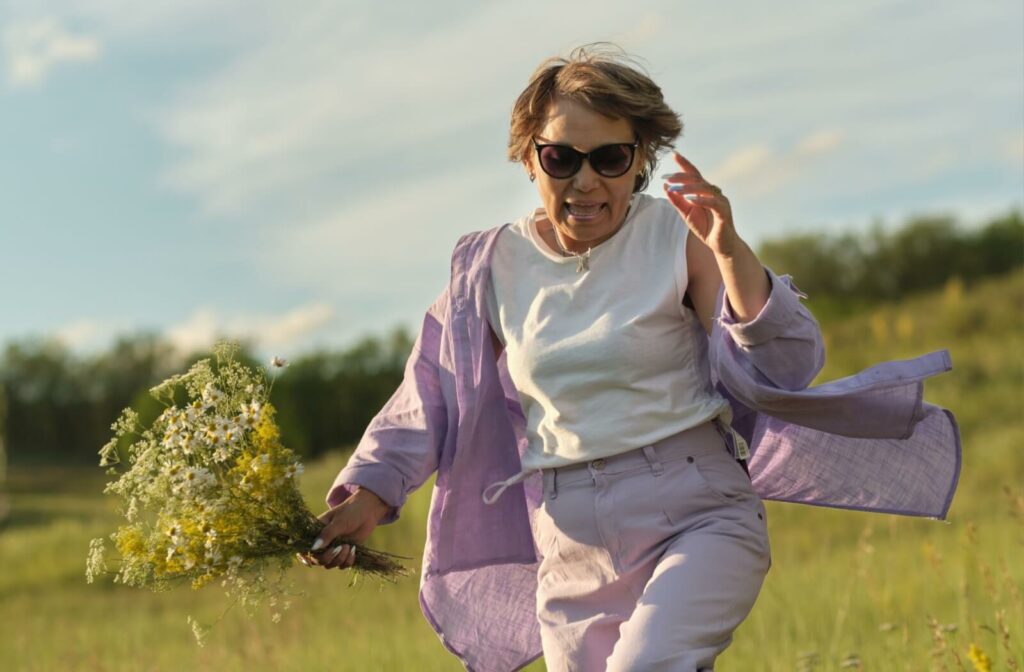 A vibrant senior skips through a field while holding a bouquet of wild flowers.