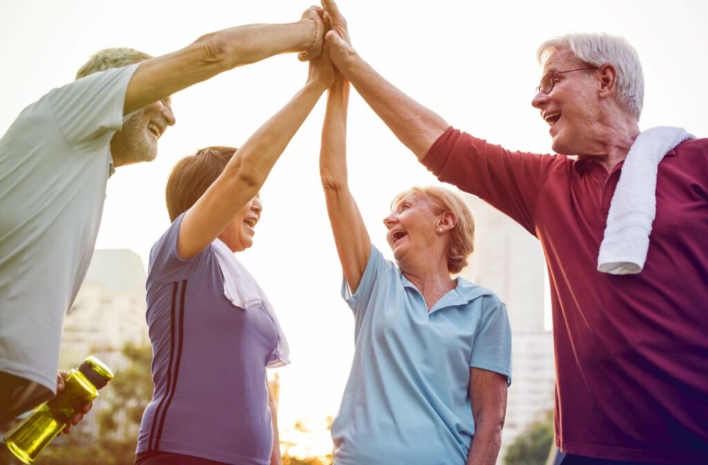 A group of laughing older adults high five each other as they finish up their group senior fitness class.