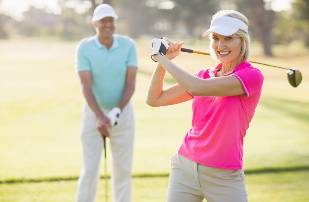 A woman swinging a golf club while another person watches on a golf course.