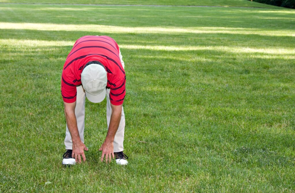 A person stretching by bending forward to touch their toes on a grassy field.