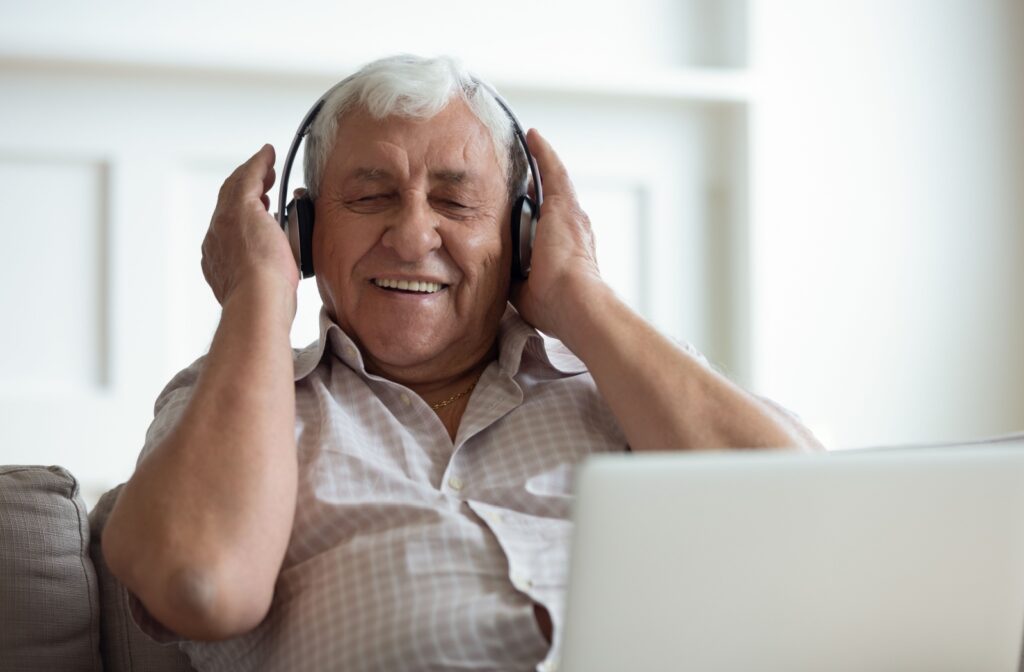 An older adult laughing while adjusting their headphones and listening to an audiobook on their couch.