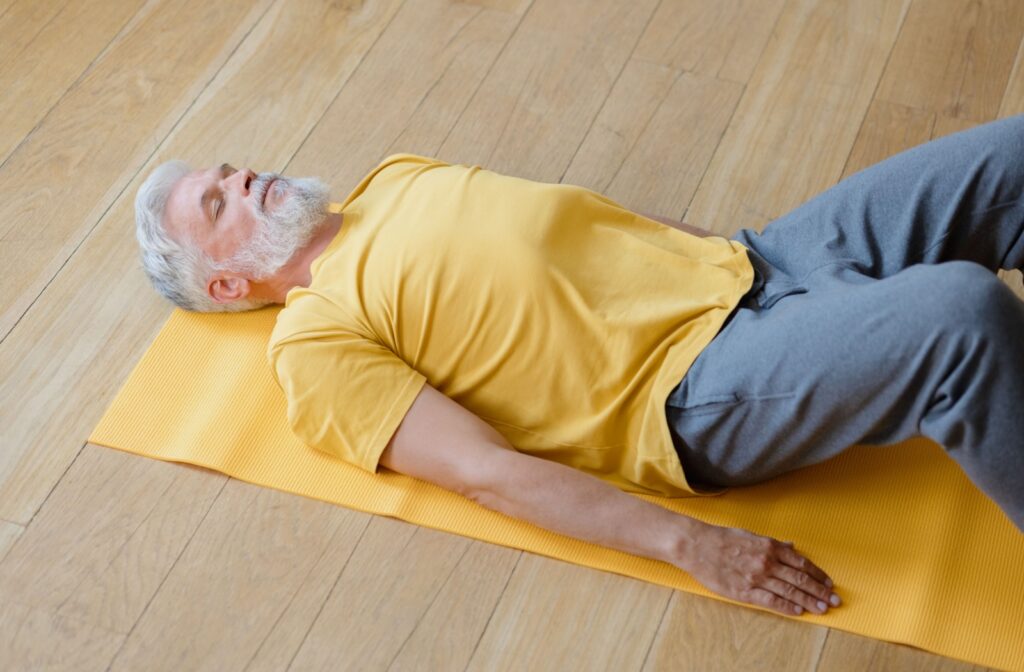 An older man lying on a mat, while performing a stretching exercise.