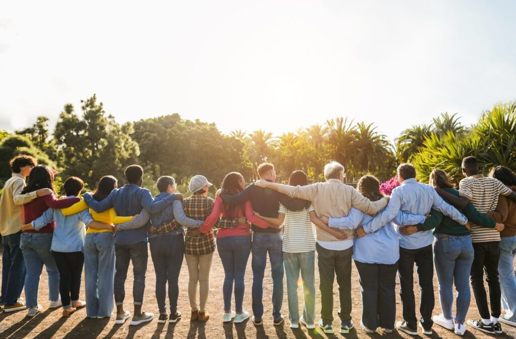 A group of multigenerational people hugging each other in a park and spending time together as a community.