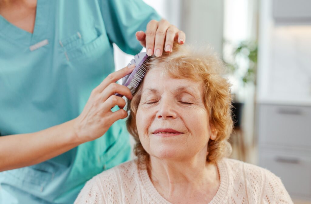 A senior getting help with brushing their hair from a caregiver at a senior living community.