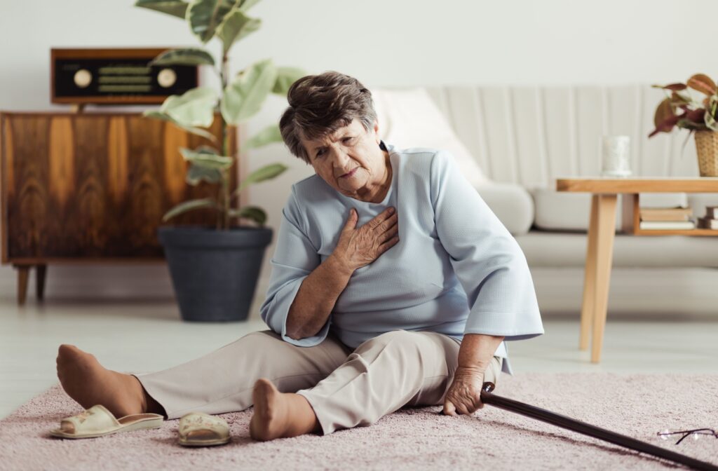 An older adult sitting on the ground in their living room, rubbing their chest in frustration after a fall.