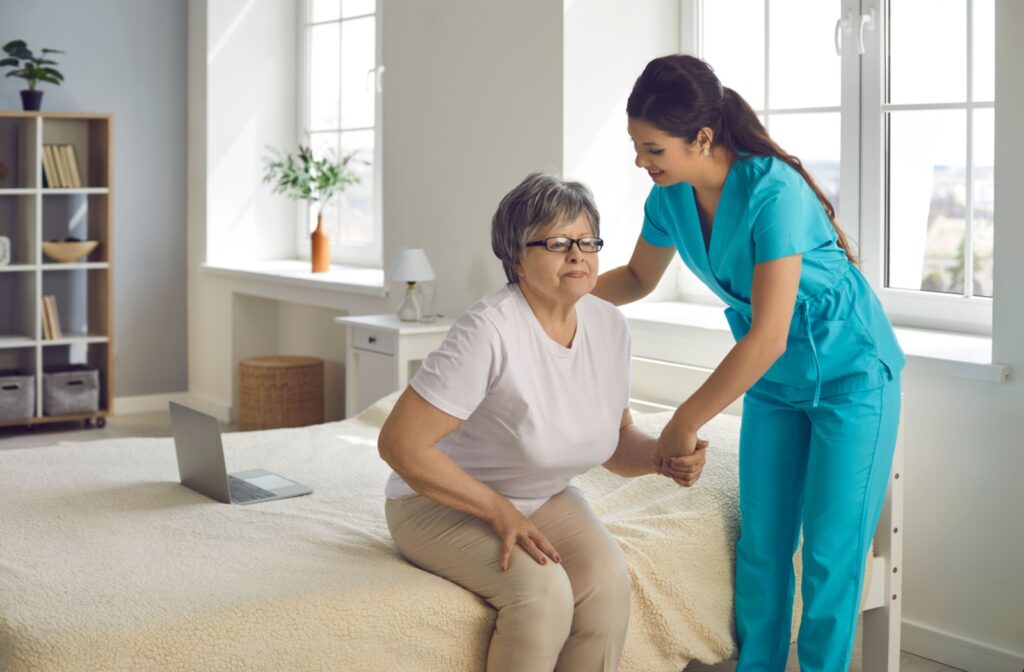 A caregiver in senior living helping an older adult stand from their bed to lower the risk of falls.