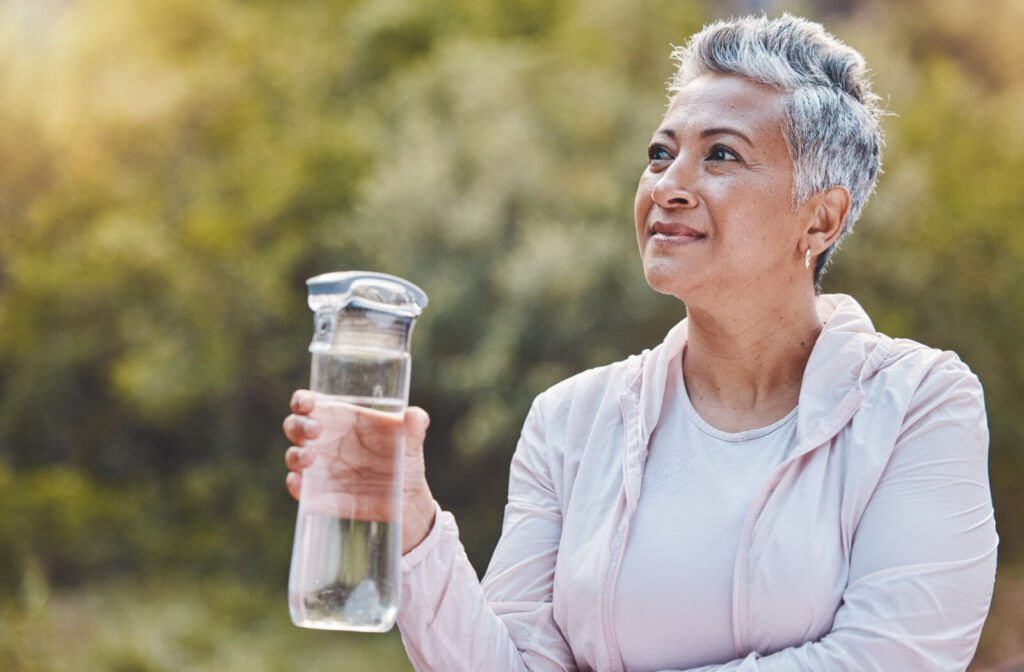 An older adult smiling and looking up at the sky while holding a clear water bottle.