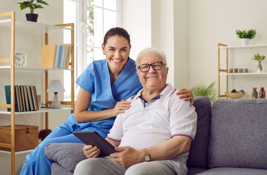 An older adult smiling and holding a tablet in assisted living while showing a caregiver a photo.