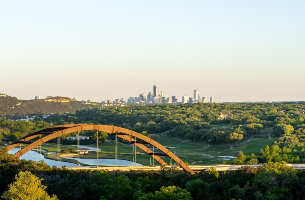 Austin skyline with Pennybacker Bridge stretching over green hills during golden hour